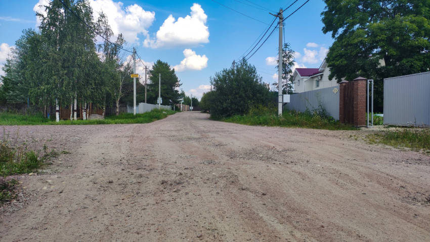 Грунтовая деревенская дорога с деревьями и забором