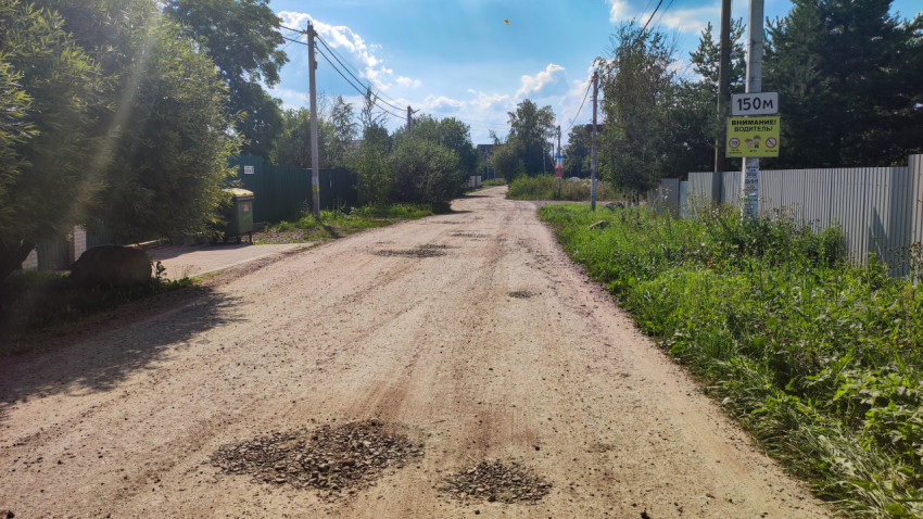 Деревенская грунтовая дорога с ямами и зелеными насаждениями