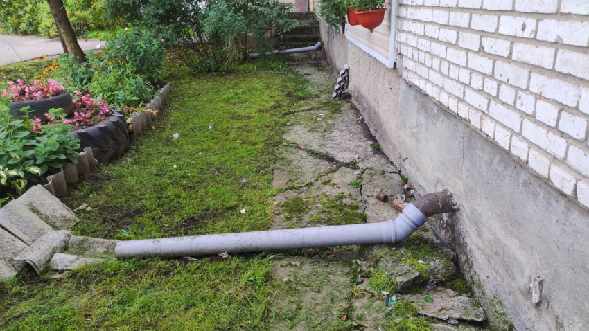 Водосточная труба рядом с отмосткой, лежащая на земле
