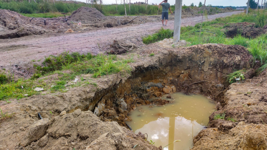 Яма с грязной водой на земельном участке среди травы и грязи