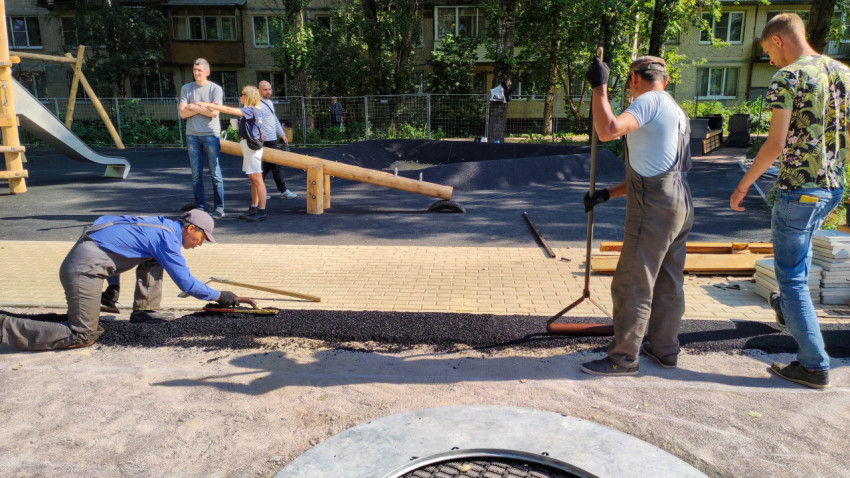 Рабочие укладывают покрытие на детской площадке