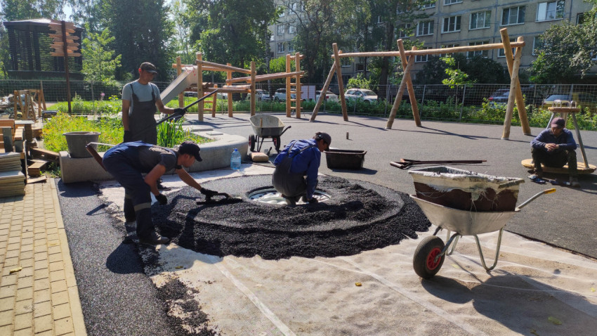 Рабочие укладывают резиновое покрытие на детской площадке