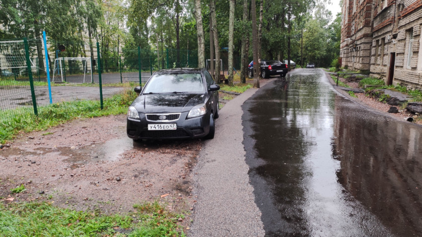 Автомобиль на обочине мокрой дороги у жилого дома после дождя