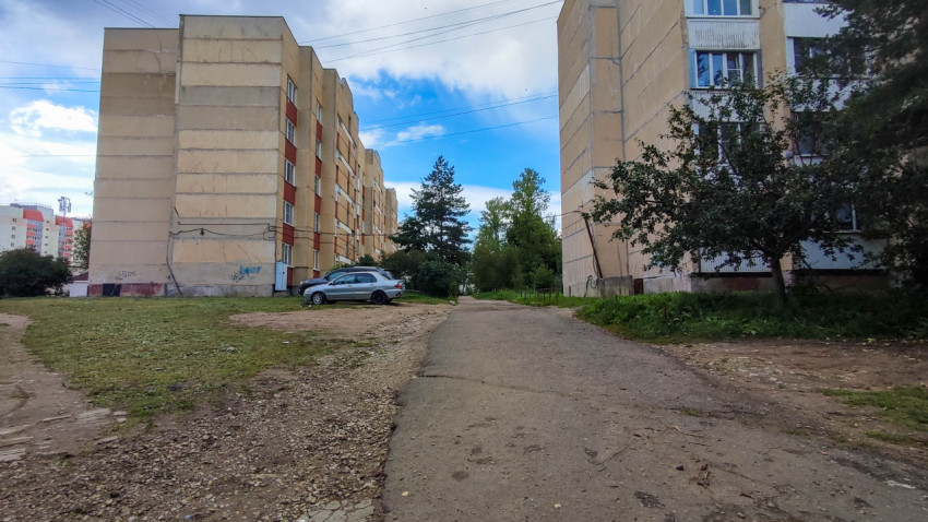 Улица между жилыми многоквартирными домами с зеленой зоной и парковкой