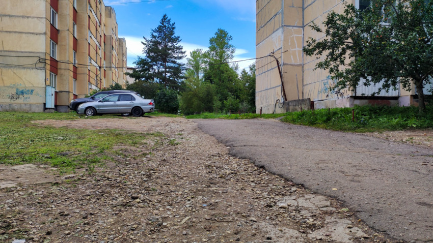 Выезд из двора с поврежденной дорогой и парковкой у жилого дома