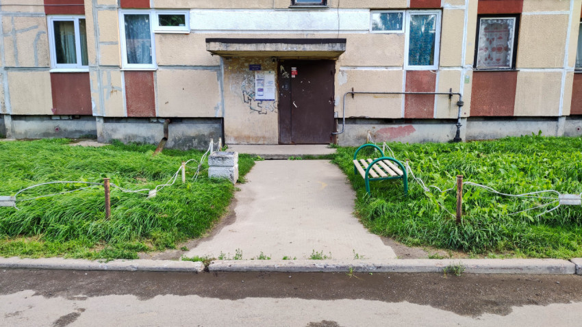 Подъезд многоквартирного дома с травяным участком, скамейкой и урной