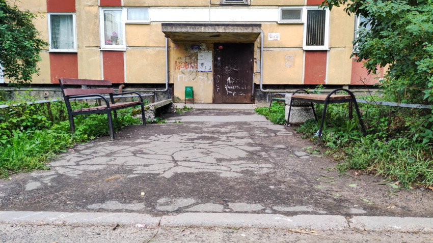 Кривой асфальтированный тротуар и скамейки у подъезда в жилом районе