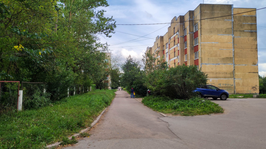 Улица в жилом районе с зелеными насаждениями и парковкой