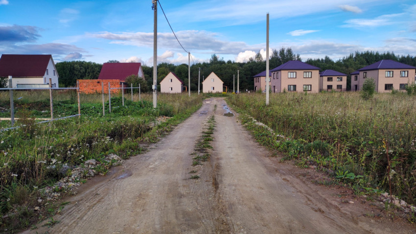 Грунтовая дорога в коттеджном поселке с электростолбами и новыми домами