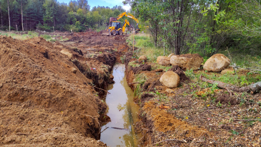 Траншея с водой и экскаватор на этапе земляных работ
