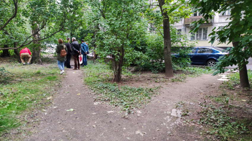 Группа людей в зелёной зоне с тропинками возле жилого дома