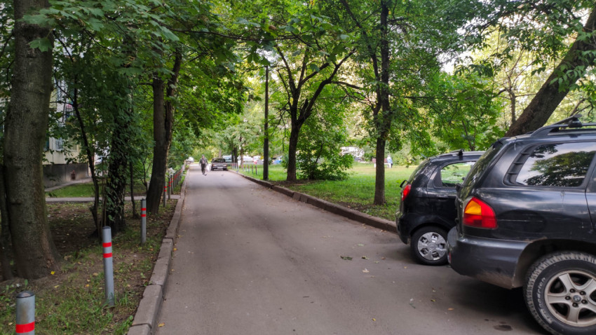 Зелёная аллея с припаркованными автомобилями и пешеходами