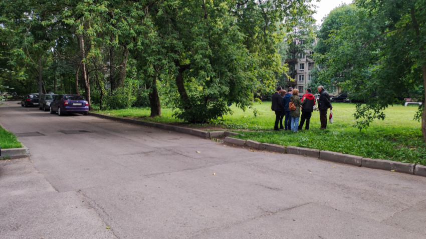 Группа людей на зелёной территории у жилого дома и припаркованные автомобили