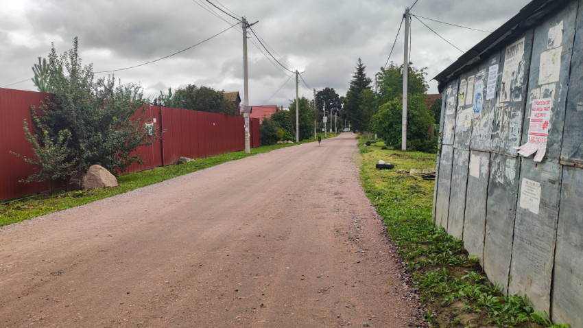 Грунтовая дорога в поселке с заборами и рекламными объявлениями
