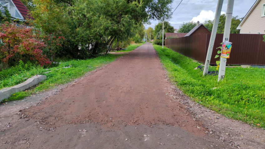 Грунтовая дорога в поселке с зелеными насаждениями и забором