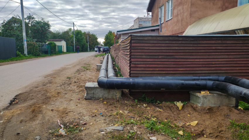 Теплотрасса вдоль деревянного забора на улице частного сектора