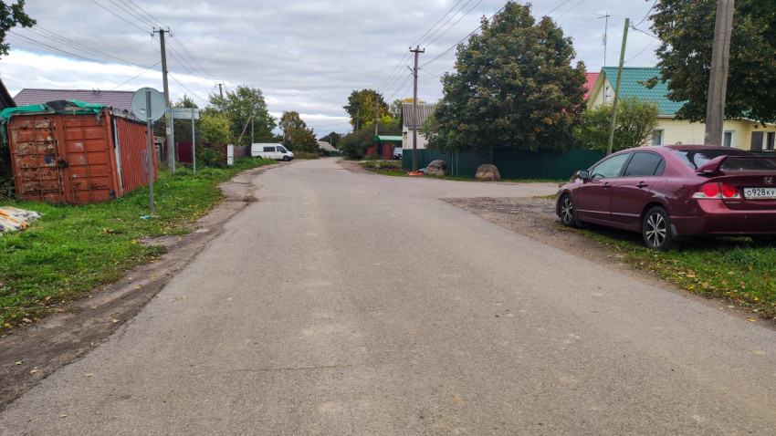 Асфальтированная дорога в частном секторе с припаркованными автомобилями и грузовым контейнером