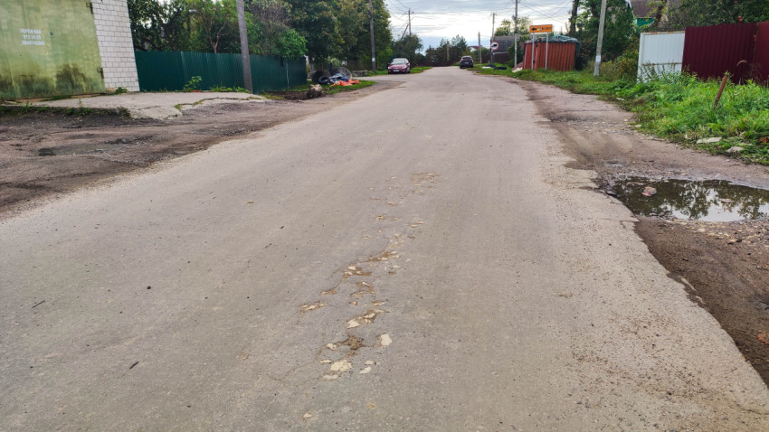 Дорога с повреждениями асфальта и лужей в частном секторе