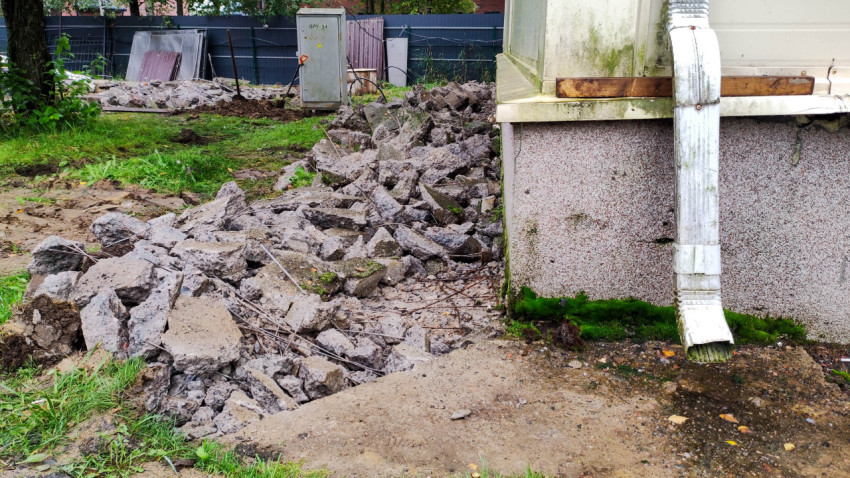 Разрушенная отмостка здания с водостоком и обломками бетона