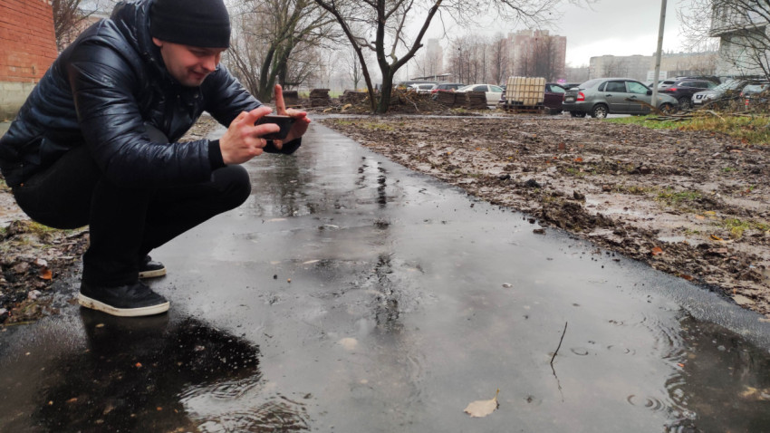 Человек фотографирует отражение в луже на асфальтированной дорожке