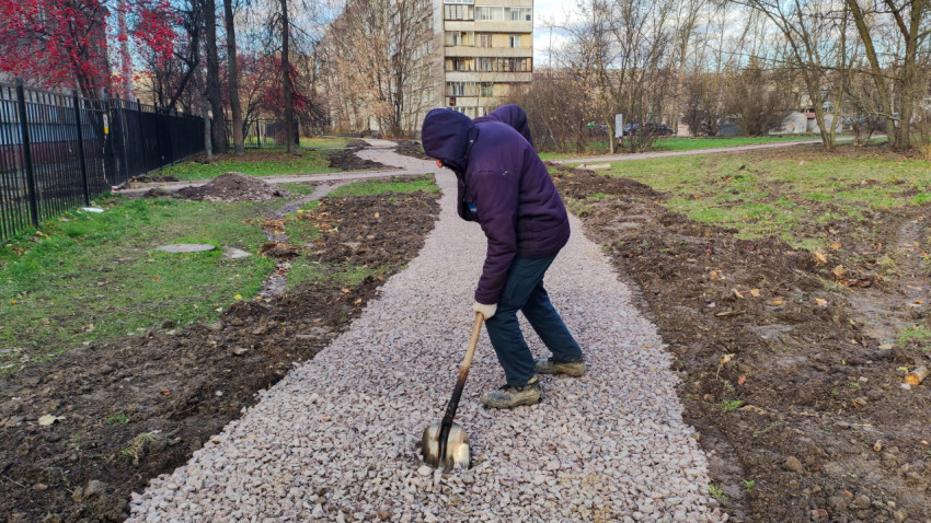 Рабочий разравнивает щебеночное основание для пешеходной дорожки