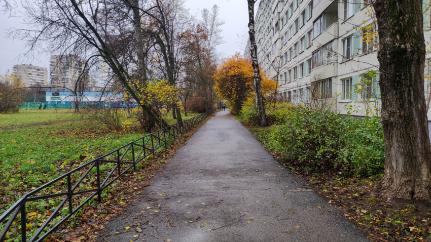 Длинная пешеходная дорожка вдоль жилого дома с осенним пейзажем