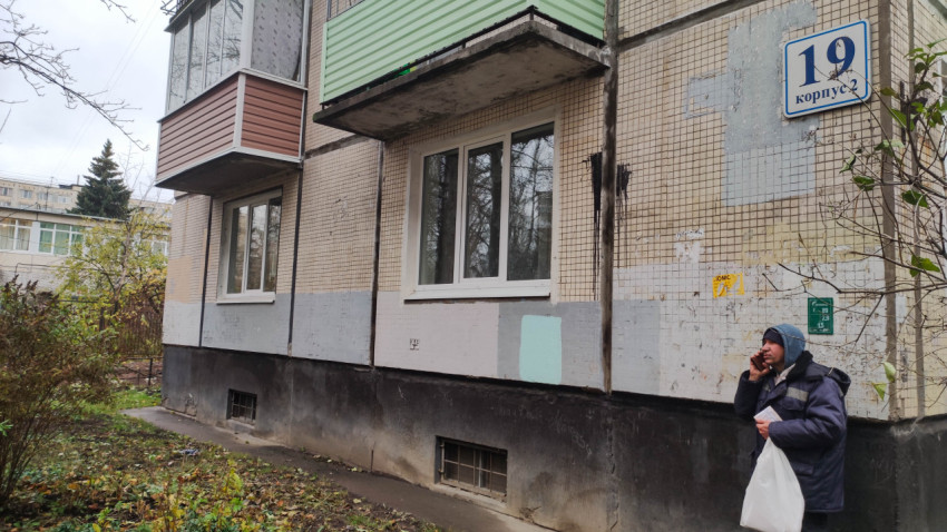 Фасад жилого дома с балконами и прохожим у стены
