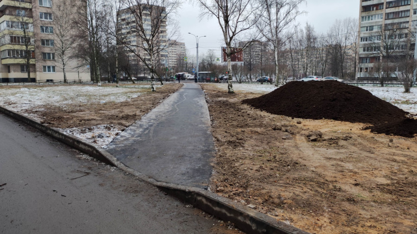 Жилой двор с новой асфальтированной дорожкой и насыпью грунта зимой