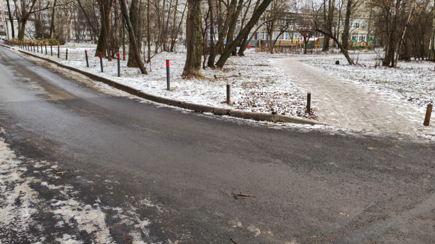 Зимний жилой двор с асфальтированной дорогой, пешеходной тропинкой и столбиками