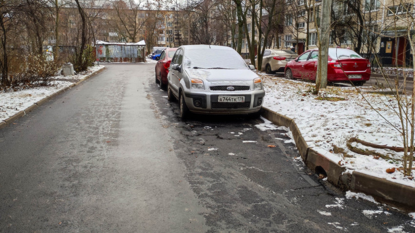 Зимняя дворовая парковка с припаркованными машинами и заснеженным асфальтом