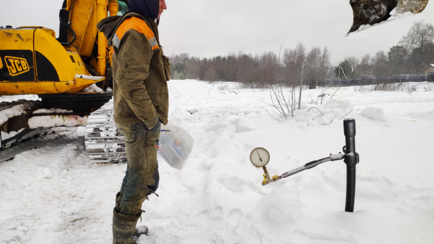 Рабочий в спецодежде на стройплощадке возле экскаватора и водопроводной трубы зимой
