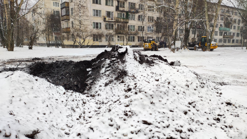 Земляные работы в жилом дворе зимой с техникой на фоне