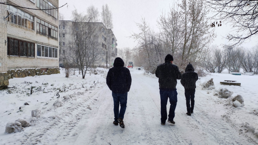 Три человека идут по заснеженной дороге во дворе жилого дома