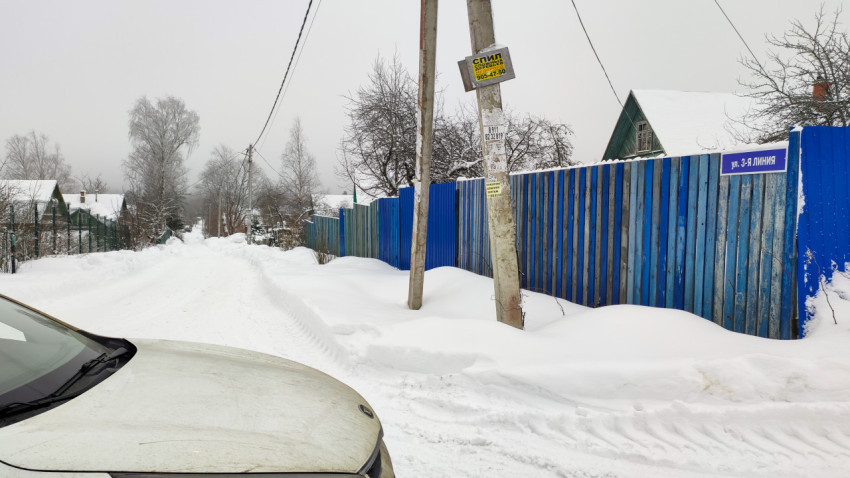 Сельская улица с синим забором и табличкой "3-я линия" зимой