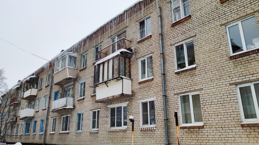 Ряд балконов на кирпичном доме с сосульками на крыше зимой