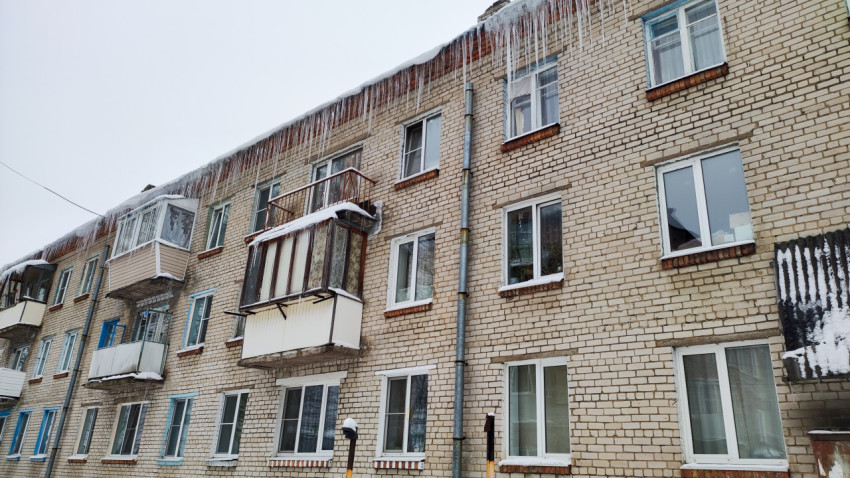 Старый кирпичный жилой дом с сосульками на крыше зимой