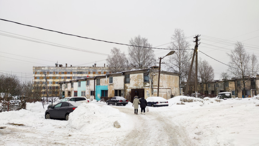 Ветхие двухэтажные дома в зимнем дворе с заснеженными автомобилями
