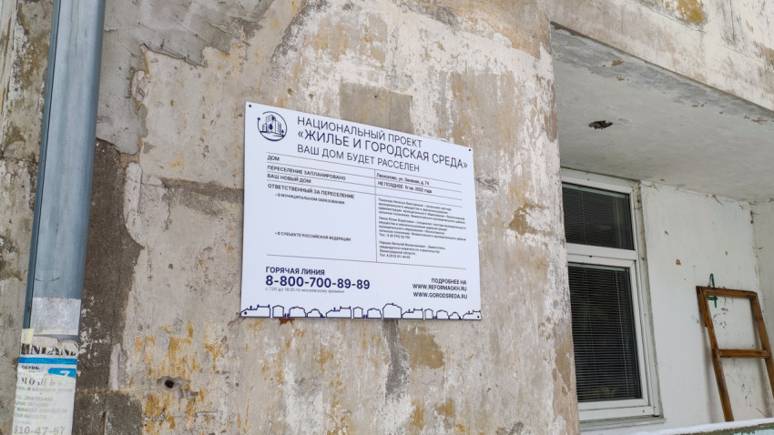 Информационный щит о переселении дома в рамках нацпроекта на обветшалом фасаде