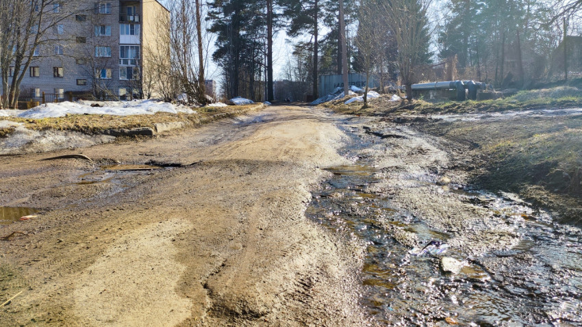 Размытая грунтовая дорога с лужами на окраине жилого квартала