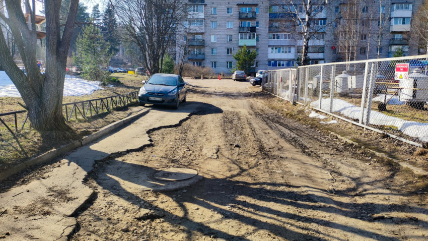 Разбитая асфальтовая дорога с припаркованными машинами