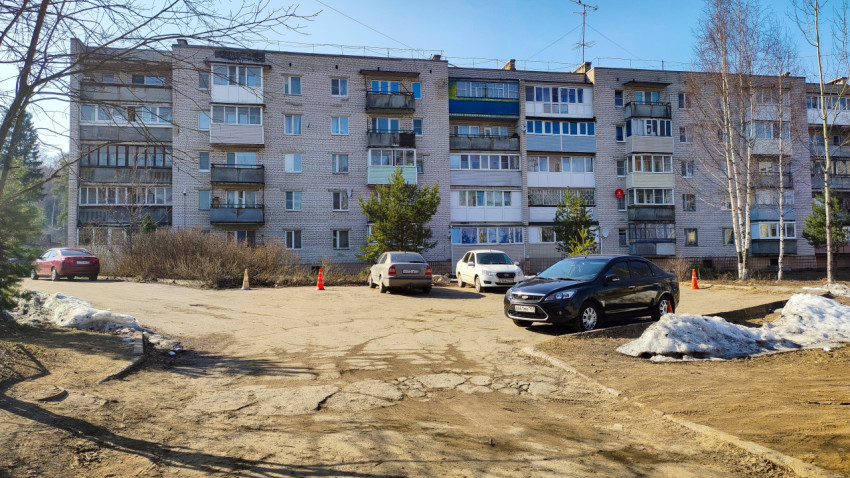 Пятиэтажный жилой дом с припаркованными машинами на фоне весеннего двора