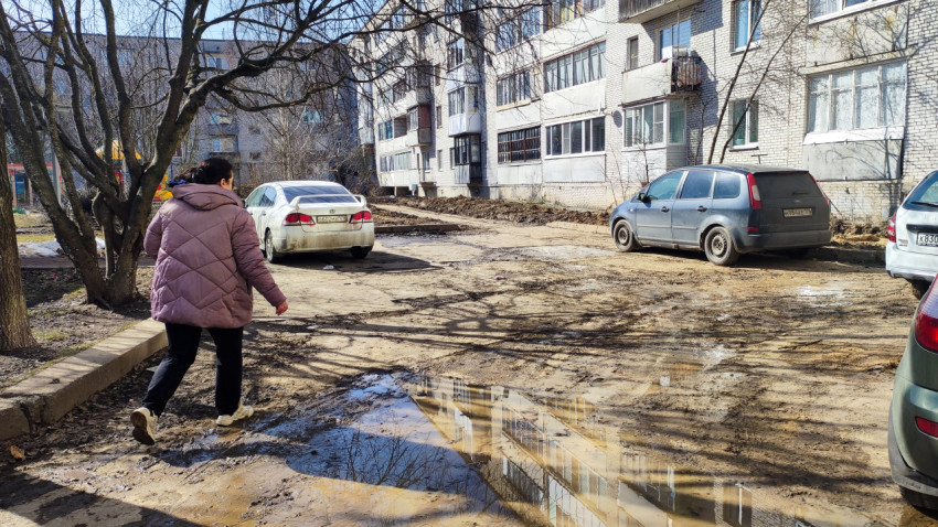 Женщина идёт по грязному двору рядом с припаркованными машинами