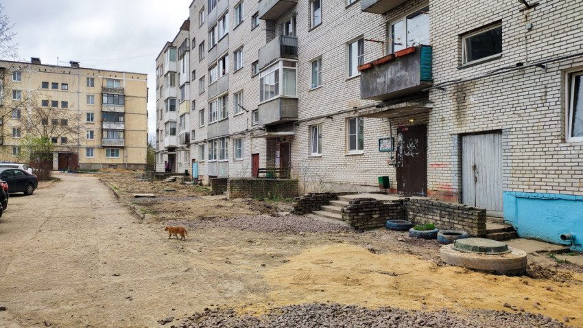 Фасад жилого дома и двор с песком и щебнем после снятия асфальта