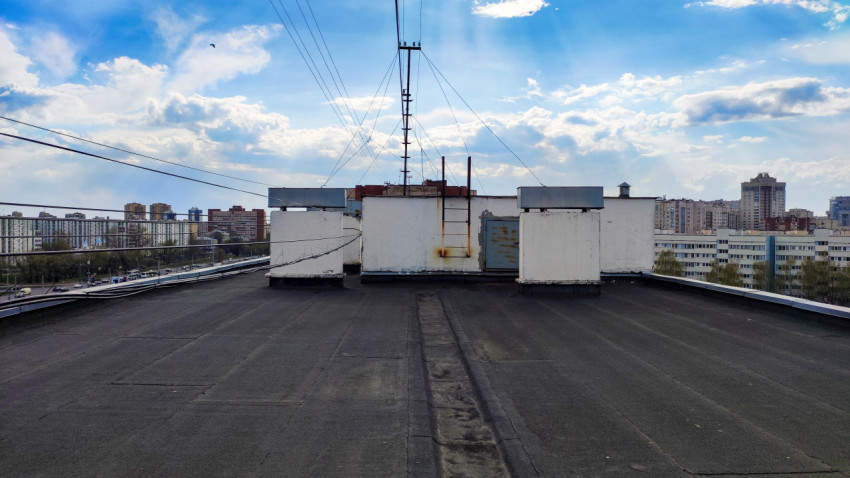 Крыша дома с люком, лестницей и городским фоном на закате