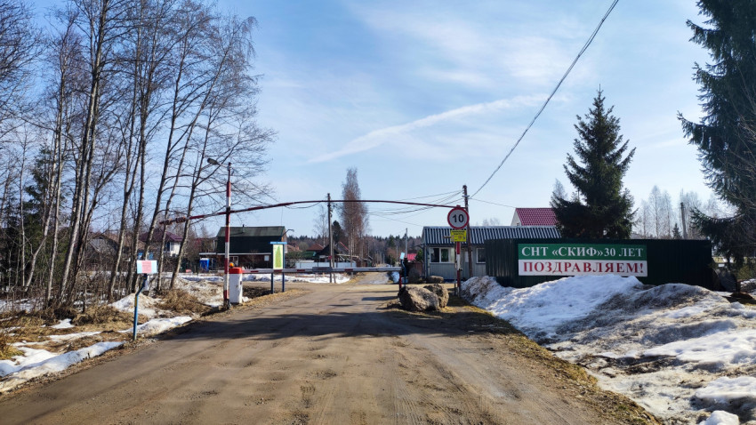 Въезд в СНТ с шлагбаумом и табличками на фоне частных домов
