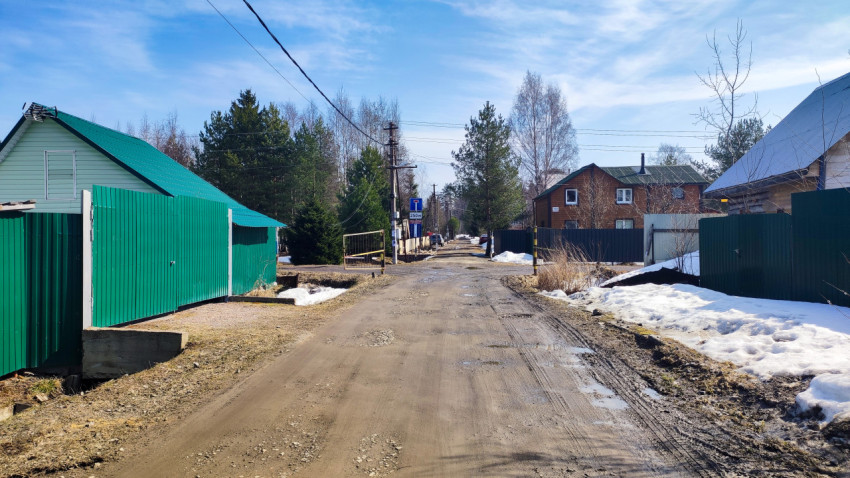 Грунтовая дорога в посёлке с зелёными заборами и сугробами