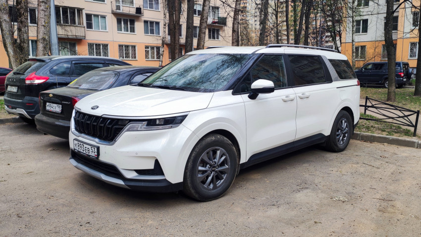 Белый минивэн Kia Carnival припаркован во дворе жилого дома