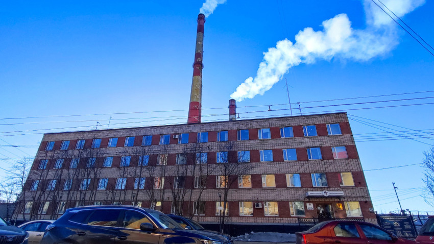 Вид на административное здание с дымящимися трубами и припаркованными автомобилями