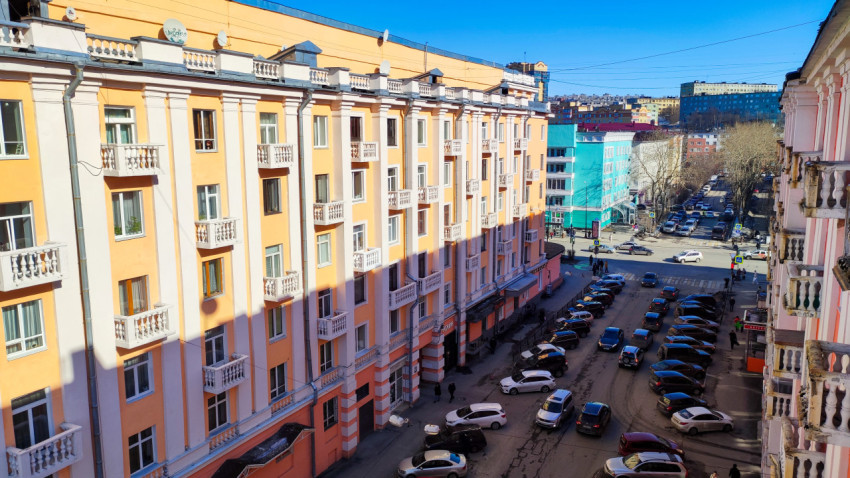 Вид на жилой дом с балконами и припаркованные автомобили