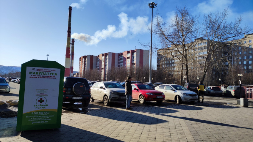 Парковка с машинами и контейнером для сбора макулатуры на фоне жилых домов